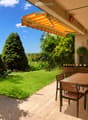 Balcony with a wooden table and chairs, surrounded by greenery and a well-maintained lawn.