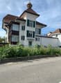 Two-story house with white walls, green shutters, red-tiled roof, and a small balcony on the left side.