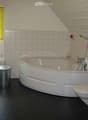 Bathroom with a bathtub, toilet, sink, and a window with blinds. The room features white tiled walls and a black floor.