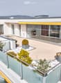 Modern rooftop terrace with glass railings, potted plants, and a view of the surrounding area.