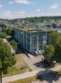Aerial view of a modern industrial building with a green roof, surrounded by trees and parked cars in a suburban area.