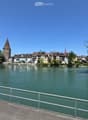 Scenic riverside view with historic buildings, a tower, and a small boat on calm water.