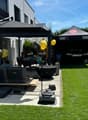 Well-maintained garden with artificial grass, patio seating area, umbrella, Weber grill, and balloons.