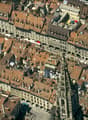 Aerial view of a historic European city with numerous buildings featuring red-tiled roofs, narrow streets, and a prominent church spire in the center.