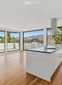 Modern kitchen with white island, wooden flooring, large windows offering a scenic view, and a range hood.