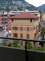 Balcony overlooking a city street with colorful buildings, parked cars, and distant mountains.