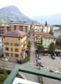 View from a balcony showing a street lined with buildings, parked cars, and a distant mountain range.