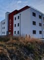 Modern multi-story building with white and red facade, located in a scenic mountainous area with a parking lot and surrounding greenery.