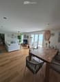 Bright living and dining area with wooden flooring, white sofa, dining table with chairs, cat furniture, and large windows leading to a balcony.