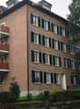 5-story building, red balconies, multiple windows, brown walls, entrance door, plant pots on balconies