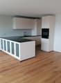 Modern kitchen with white cabinets, black countertop, and wooden flooring.