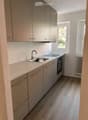 Modern kitchen with light grey cabinets, a double sink, and an oven. The space features light-colored countertops and a wooden floor.