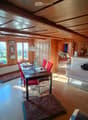Cozy dining area with wooden ceiling, large windows, and a dog present. Includes a dining table with chairs, a lamp, and decorative items.