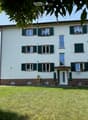 Multi-unit apartment building with white exterior, green shutters, and a garden in the front.