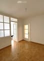 Empty room with wooden flooring, large frosted windows, and two open doors leading to other spaces.