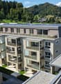 Modern multi-story residential building with solar panels on the roof, surrounded by greenery and a scenic landscape.