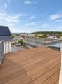 Wooden deck with metal railing, overlooking a suburban neighborhood with houses, trees, and a clear blue sky.