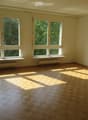 Empty room with wooden flooring and large windows allowing natural light to enter, with radiators beneath the windows.