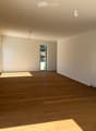 Empty room with wooden flooring, white walls, and built-in cabinets. Natural light streams in from a large window and a door leading outside.