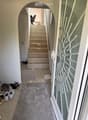 Hallway with a staircase leading upwards, a glass door with decorative pattern on the right, and a gray rug on the floor. Shoes and slippers are placed near the entrance.