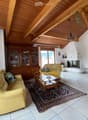 Living room with exposed wooden beams, cream-colored sofas, coffee table, cabinet, table lamp, television, fireplace, and chandelier.