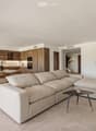 Modern living and dining area with a large sectional sofa, coffee table, dining table with chairs, and a kitchen area with wooden cabinets and appliances.
