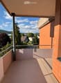 Balcony with metal railing, pink floor, overlooking a residential area with houses, trees, and a mountain in the background.