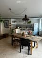 Open-plan kitchen and dining area with wooden flooring, a large wooden dining table with chairs, pendant lighting, and various kitchen appliances and decor.