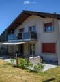 Two-story house with a modern design, featuring a balcony on the upper level, a patio with outdoor furniture, and a well-maintained garden.