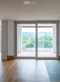 Bright, unfurnished room with wooden flooring, large windows, and a sliding glass door leading to a balcony with scenic views.