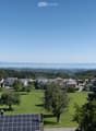 A panoramic view of a suburban neighborhood with houses, green lawns, trees, and a distant body of water under a clear blue sky.