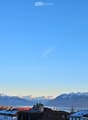 Panoramic view of a town with snow-capped mountains and a lake in the background under a clear blue sky.