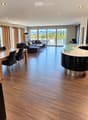 Open-plan living and dining area with modern furniture, wooden flooring, large windows offering a scenic view, and a sleek kitchen island.