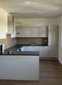 Modern kitchen with white cabinets, black countertop, and wooden flooring. Features a sink, stove, and various small items on the counter.