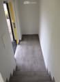 A clean, modern hallway with grey tiled flooring and white walls, featuring a staircase leading upwards and an open doorway to the left.