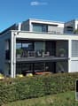 Modern multi-story house with a raised ground floor, two balconies, garden, and covered terrace.