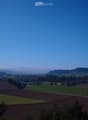 Panoramic view of a rural landscape with fields, scattered trees, and distant hills under a clear blue sky.