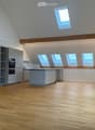 Bright, open kitchen with wooden flooring, modern grey cabinetry, and multiple skylights providing natural light. The space is completely empty, with no furniture or appliances visible.