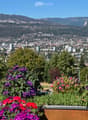 Balcony with vibrant purple and red flowers, overlooking a cityscape with buildings and distant mountains.