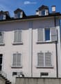 Two-story residential house with light pink facade, multiple windows with shutters, and a small balcony on the first floor.