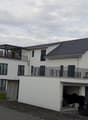Modern two-story white house with multiple balconies, garage, and a parked car in front.