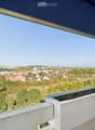 Balcony with a retractable awning, overlooking a cityscape with trees, buildings, and distant mountains.
