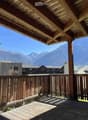 Wooden balcony with a railing, overlooking a scenic mountain view and neighboring houses.