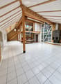 Bright, open room with white tiled flooring, wooden beams, and large windows. The space is empty, with no furniture or furnishings visible.