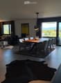 Modern living and dining area with large windows offering a scenic view, featuring a sofa, coffee table, ottoman, dining table with chairs, and decorative vases.