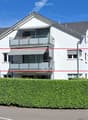 Two-story modern house with white exterior, grey roof, multiple windows, and balconies.