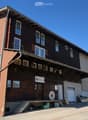 Two-story wooden building with brick and wood siding, multiple windows, balconies, and a sign reading "MÜHLE".