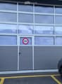 Gray building, large garage doors, 'Passage Interdit' sign, small pedestrian door, yellow parking lines