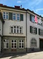 A two-story building with a light-colored facade, multiple windows with shutters, and a sign reading "NORTHILING" above the entrance. Two flags are displayed on the right side of the building.