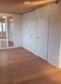 Empty room with light wooden flooring, white walls, and a large mirrored wardrobe unit. The room has a door leading to another space and a radiator on the left side.